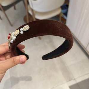 Detailed close-up of dark brown velvet headband with ruby red gemstone and pearls