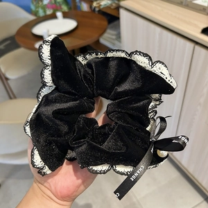 Detail of black velvet scrunchie with white lace trim, pearl bead, and lettered ribbon