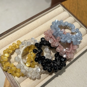 Five opal-effect elastic hair ties in pastel colors displayed on a beige velvet tray