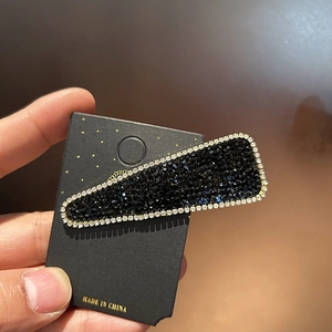 Elegant black rhinestone hair clip with white crystal border on a display card