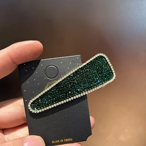 Sparkling green rhinestone hair clip with gold trim on a black display card