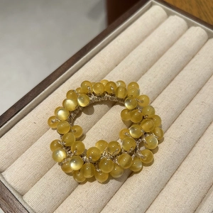 Detail of amber cat eye beaded hair tie with gold wire on beige velvet box