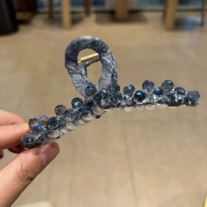 Detail view of a large blue fabric hair claw clip with sparkling beads and gold spring