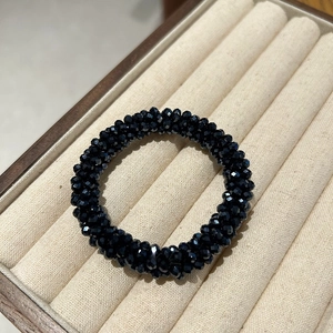 Macro detail of elastic hair tie featuring multifaceted black crystal beads on beige velvet
