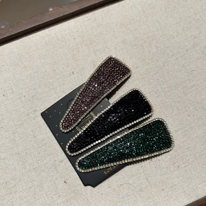 Detailed macro view of three teardrop rhinestone hair clips in burgundy, black and green