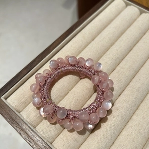 Detailed close-up of pink opal-style beads on a woven elastic hair tie on a beige tray