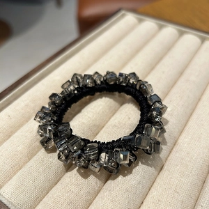 Close-up of grey crystal cube beads on thick elastic hair tie shown on a beige tray
