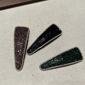 Detailed close-up of three sparkling rhinestones hair clips in purple, black and green