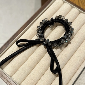 Detailed close-up of an elastic hair tie featuring a faceted gray crystal and black ribbon