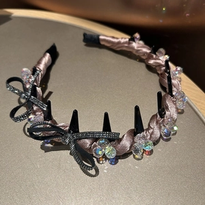 Close-up of pink satin headband featuring black rhinestone bow and decorative crystals