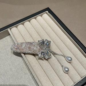 Détail d'une pince à cheveux argentée avec strass roses, perles et glands suspendus
