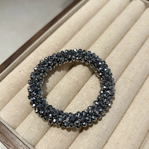Detailed close-up of dark grey faceted crystal beads hair tie on a beige velvet tray