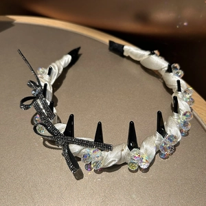 Close-up of white silk headband featuring black spikes, iridescent beads and rhinestone bow