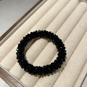 Macro shot of faceted black crystal beads on a flexible elastic hair tie in jewelry tray