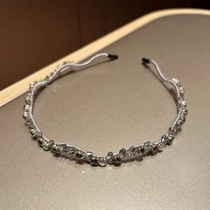 Detail eines eleganten gewellten Haarreifs mit grauen Kristallen und Goldperlen