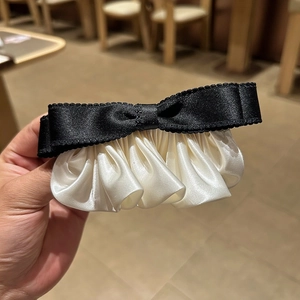 Détail d'un nœud en satin noir élégant avec pince à cheveux en tissu plissé crème