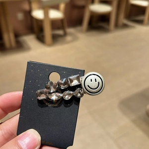 Glittering silver smiley face hair clip with various rhinestones on black card