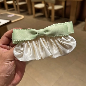 Détail du nœud en ruban vert clair et plis de satin crème sur une barrette à cheveux