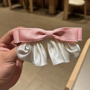 Détail de la pince à cheveux nœud en satin rose et crème aux bords ondulés élégants