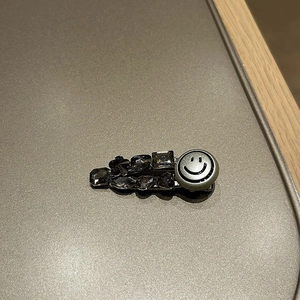 Detailed close-up of a silver hair clip featuring grey rhinestones and a metal smiley face