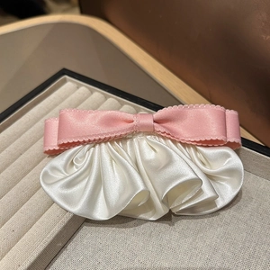 Gros plan sur la barrette à cheveux nœud en satin rose et blanc dans un écrin beige élégant