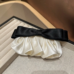 Détail de la pince à cheveux avec nœud en satin noir et plis en soie crème