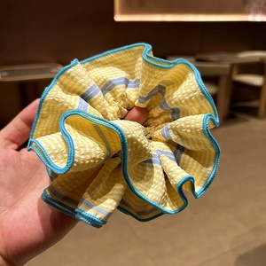 Détail d'un chouchou en tissu à rayures jaunes avec bords bleus cousus et texture élastique