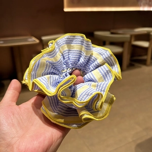 Détail d'un chouchou à rayures bleues et blanches avec bordure ondulée jaune en tissu