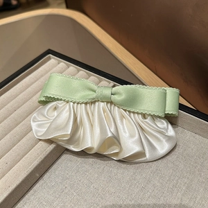 Gros plan d'une pince à cheveux élégante avec nœud vert clair, bords dentelés et plis satinés