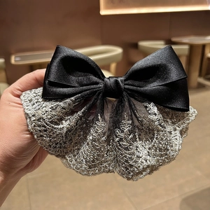 Detail of elegant black satin bow hair clip with embroidered gold lace textures