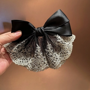 Detail view of chic black satin bow with vintage beige lace embroidery and leaf patterns