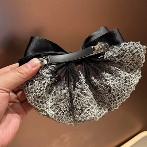 Detail of black satin bow hair clip with intricate silver lace embroidery and metal spring clip