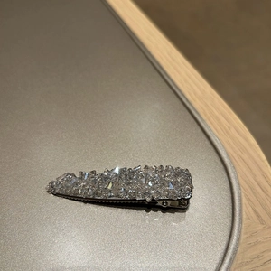 Macro detail of silver duckbill clip with sparkling pavé crystals on a minimal surface