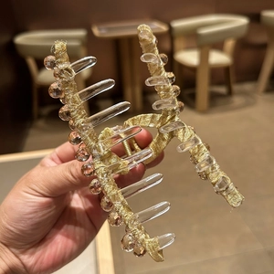 Détail d'une grande pince à cheveux en tissu doré avec perles en cristal ambre et dents acryliques