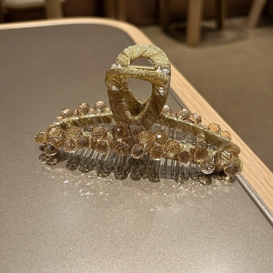 Gros plan détaillé des perles de cristal champagne sur la pince à cheveux dorée tissée
