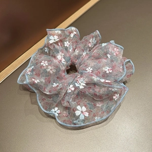 Détail du chouchou en organza floral avec imprimés pastel et bords roulés bleu clair
