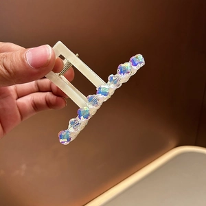 Détail d'une pince à cheveux blanc crème avec cristaux carrés colorés aux reflets irisés
