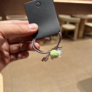Detail of high-elastic coffee hair tie with green striped bead and clear flower charm