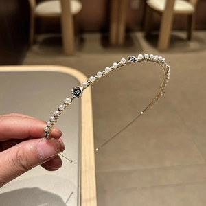 Dettaglio di un cerchietto dorato con perle bianche e ciondoli a quadrifoglio nero e strass
