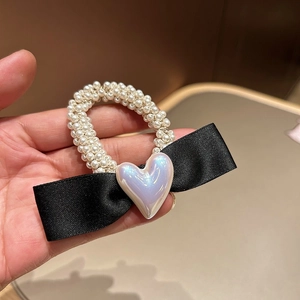 Détail d'un élastique en perles avec un nœud en satin noir et une perle en cœur