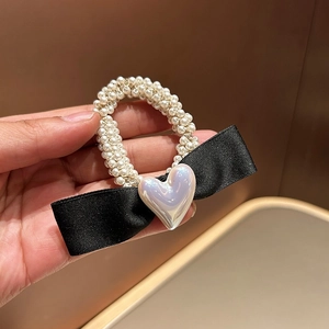 Détail d'un nœud en satin noir et perles blanches sur un élastique à cheveux chic