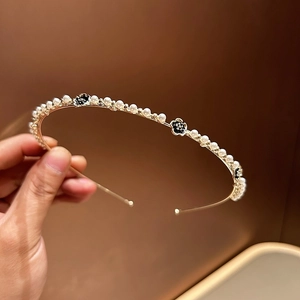 Dettaglio del cerchietto dorato con perle bianche e accenti di fiori in smalto nero