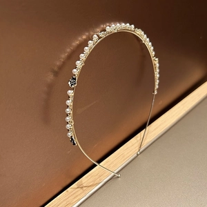 Elegante cerchietto in metallo dorato con perle bianche e dettagli floreali su legno
