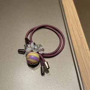 Close-up of dual-strand purple hair tie with faceted crystal beads and striped round charm