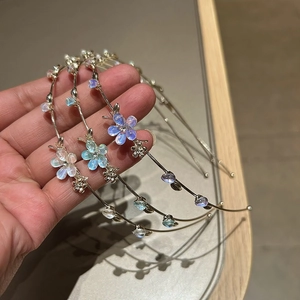 Détail de trois serre-têtes en alliage avec fleurs irisées et strass tenus à la main
