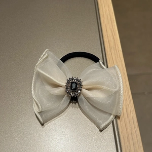 Macro shot of an elegant cream organza bow hair tie with a vintage black gemstone center