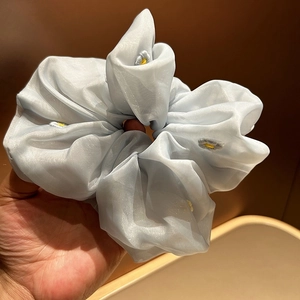 Detail of light blue organza scrunchie with delicate daisy floral embroidery texture