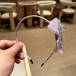 Macro detail of purple organza ribbon bow with sparkling rhinestones on slim metal headband