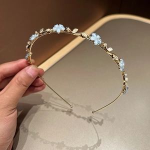 Détails d'un serre-tête en métal doré orné de fleurs bleues et de perles brillantes