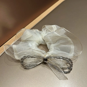 Close-up of white organza scrunchie with gold glitter edges and crystal beaded bow